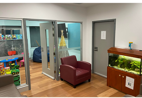 A room with 3 armchairs and a fish tank. There is a glass wall and door leading into another room with children’s toys and furniture.