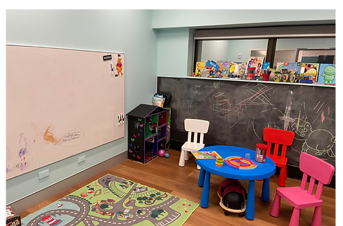 A children's waiting area with a small plastic table and 3 matching chairs. There is a rug on the floor, a white board on one wall and a chalkboard on the other wall.